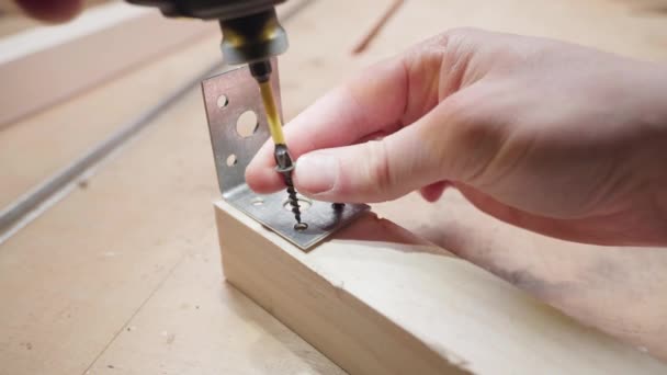 Screwing a metal corner to a wooden bar with self-tapping screws using an electric screwdriver — Vídeo de Stock