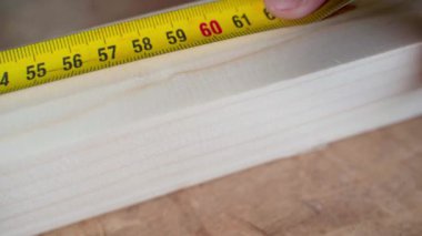 Yellow ruler tape measure measures a wooden bar close up, black pencil mark