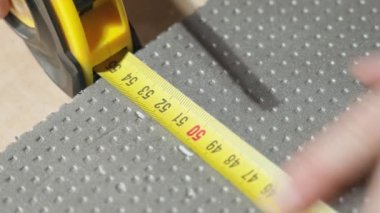 Measuring the dimensions of gray thick insulation foam using a yellow tape measure close-up. Marks with a pencil
