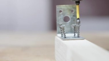 Siyah kendini beceren vidaları metal bir köşeyi yakın plan bağlamak için tahta bir çubuğa sokuyor.