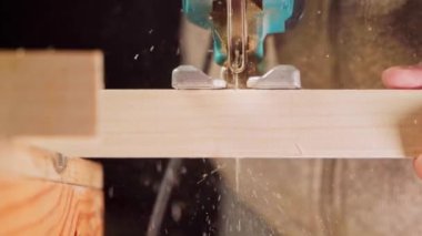 Tahta kirişi yakın çekimde testereyle keserken talaş ağır çekimde uçuyor.