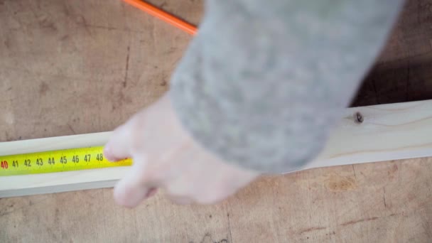 Tangan mengukur panjang batang kayu dengan pita kuning dan membuat tanda dengan pensil close-up, top view — Stok Video
