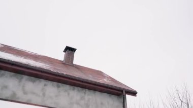 Küçük bir özel evin çatısı bulutlu bir gökyüzünün arka planına karşı karla kaplıdır.