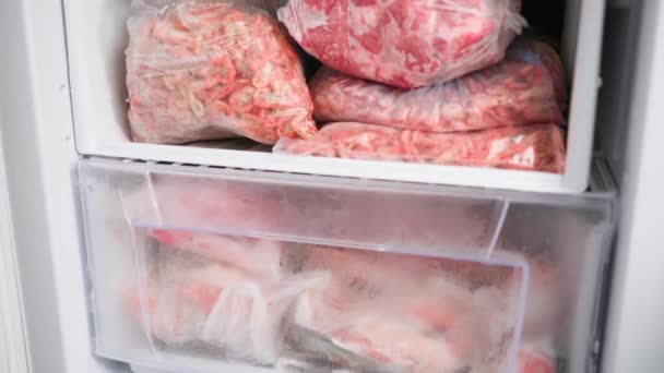 The freezer shelves are crammed with packages of frozen meat products and shrimp — Stock Video