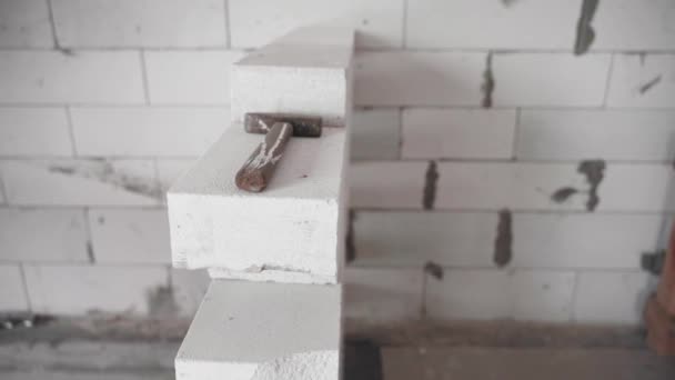 De hamer ligt op een onafgewerkte witte bakstenen muur close-up. Een huis bouwen van een gasblok — Stockvideo