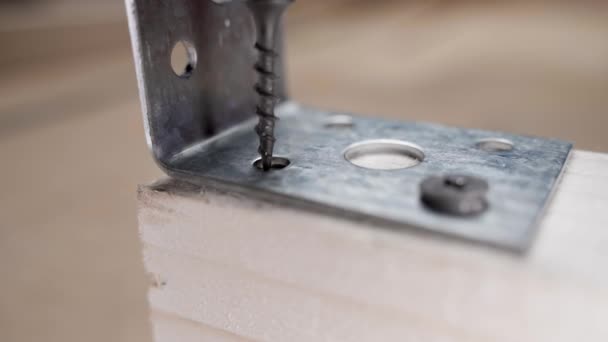 Fijación de un ángulo de hierro a una viga de madera con un tornillo autorroscante negro de cerca — Vídeo de stock