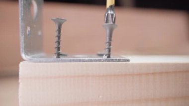 Tornavidalar kendi kendine vurulan siyah vidayı yakın plan tahta bir bloğa saplar. Demir köşeyi ahşap parçalara bağlıyorum.