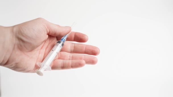 Una mano aprieta una jeringa médica con una aguja cerrada sobre un fondo blanco — Vídeo de stock