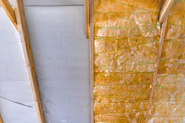 Cam yünden önce ve sonra çatı yalıtımı. Yığınların arasından hidrobariyere kadar sarı cam yünler seriliyor.