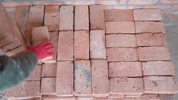 Una mano guantata impila mattoni di ceramica rossa anche. Lavorare in un cantiere — Video Stock