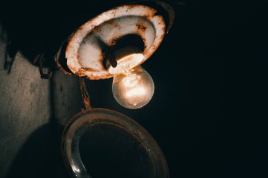 Bodrumda paslı bir tabanı olan eski bir cam gölgede eski bir parlak ampul parlıyor.