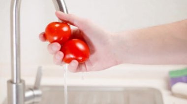 Yıkanmış kırmızı domatesleri sallıyor ve suyu kapatıyor.