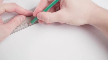 Eller beyaz bir kağıt üzerine şeffaf bir plastik cetvel koyar ve yakın plan kalemle çizgiler çizer.