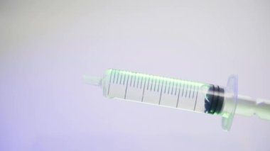 Renkli ışıklandırmanın altında beyaz arka planda şeffaf sıvı yakın plan şırınga. İğnesiz tıbbi şırınga