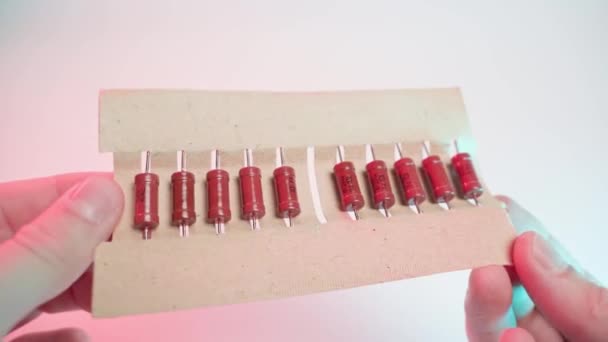 Staré oranžové rezistory zavřít v papírové balení v rukou na bílém pozadí, detailní záběr v barevném osvětlení — Stock video