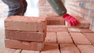 Kırmızı eldivenli inşaatçı kırmızı seramik tuğlaları düzgünce istifliyor.