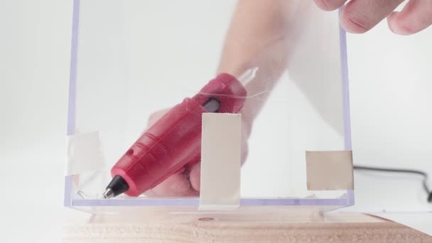 Self-gluing transparent plexiglass with a red glue gun on a white background. Handmade, transparent plastic cube — ストック動画