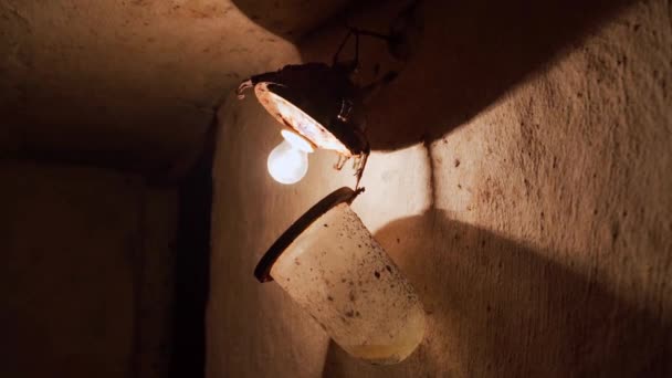 An old incandescent light bulb in an old lampshade with a glass cover in an underground basement. Cellar lighting — Vídeos de Stock