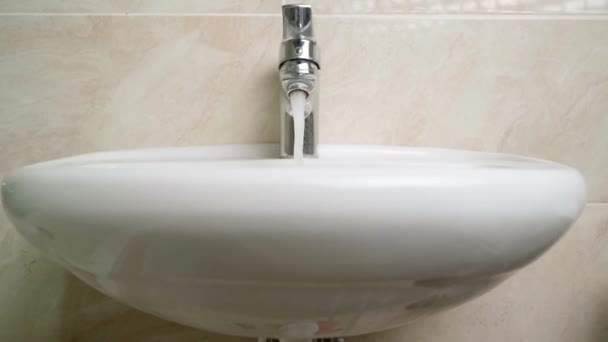 We slowly approach the washbasin with water flowing from the tap into the drain hole close-up — Vídeo de Stock