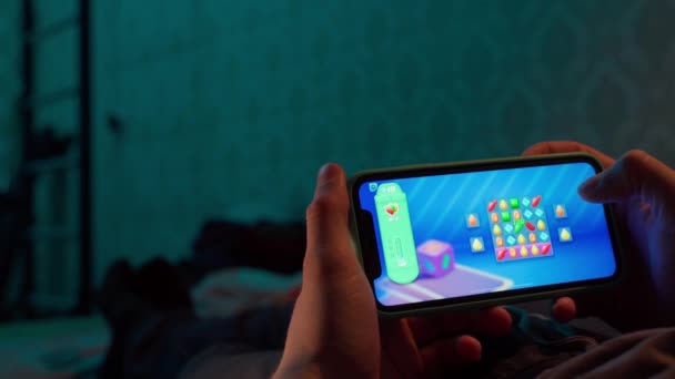 Киев, Украина - 23 марта 2022 года: Руки, играющие в мобильную игру конфетная содовая по телефону вечером лежа на кровати в темноте — стоковое видео