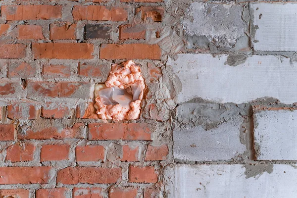 The hole in the wall was filled with foam. Wall made of red brick and aerated concrete block