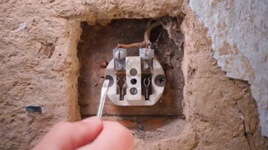 Bending terminals in a disassembled wall socket. Fixing an old socket in a clay wall with a screwdriver, close-up. High quality 4k footage