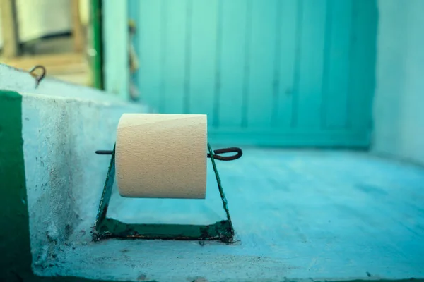 A roll of the cheapest single ply toilet paper on a toilet paper holder in a rural outdoor toilet