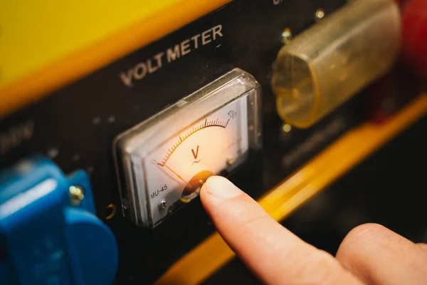 Voltmeter on the body of the gas generator close-up. The finger points to an electrical measuring device. Electromechanical voltmeter shows zero
