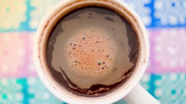 Top view of a cup of coffee on a colored background. Coffee foam swirls after mixing close-up. High quality FullHD footage