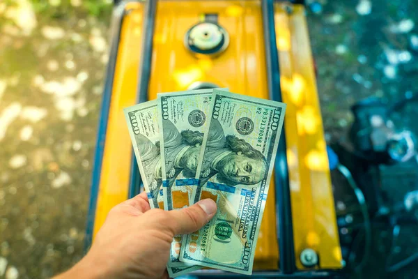 Buying a gasoline generator for dollars. A hand holds three one hundred dollar bills against the background of a new yellow gas generator