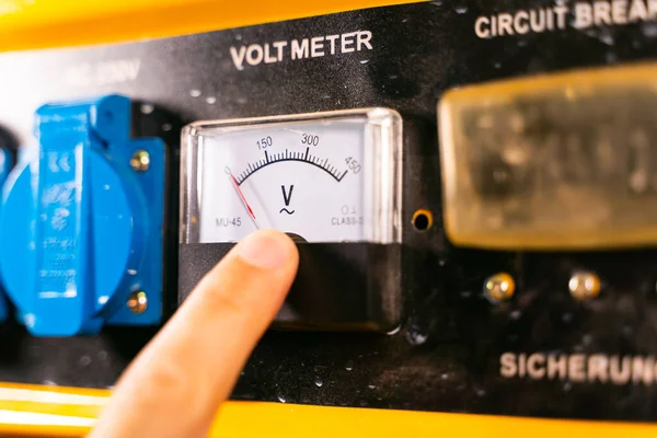 Voltmeter on the body of the gas generator close-up. Finger points to an electrical measuring device
