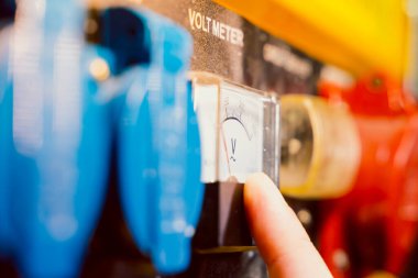 Gaz jeneratörünün gövdesinde voltmetre var. Parmaklar bir elektrik ölçüm cihazını işaret ediyor.