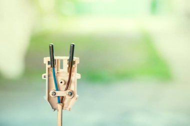 Bir elektrikli aletin kablolarını bir elektrik prizine bağlamak. Renkli bulanık bir arka planda parçalanmış beyaz plastik elektrik prizi yakın plan. Kahverengi ve mavi kablo.