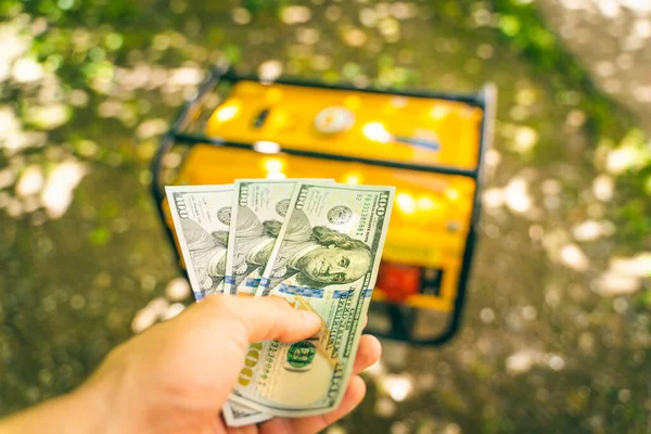 Buying a gasoline generator for dollars. A hand holds three one hundred dollar bills against the background of a new yellow gas generator