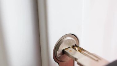 A perforated key is inserted into the keyhole of a white plastic door close-up in slow motion. High quality FullHD footage