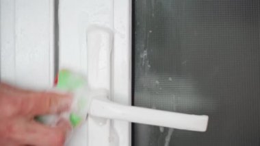 A hand thoroughly cleans white plastic doors with a sponge and foam detergent close-up. High quality 4k footage