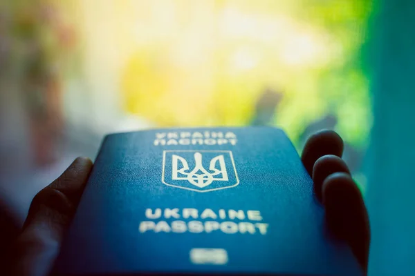 Ukrainian biometric passport in hand close-up on a blurred background. Coat of arms of Ukraine in the form of a trident. Blue document proof of identity and citizenship of a Ukrainian
