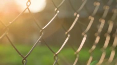 Sunbeams of the morning rising sun make their way through the chain-link fence. Movement along the fence, close-up with a blurred background. High quality FullHD footage
