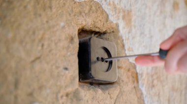 Unscrewing the black housing of the wall socket with a screwdriver. Old building with poor repair and clay brown walls. High quality 4k footage