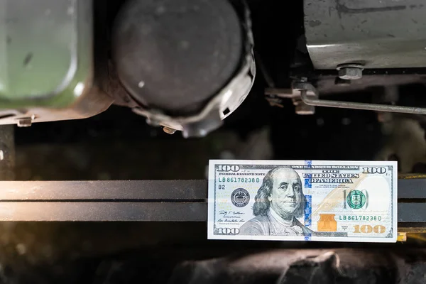 Hundred dollar bill close-up on an industrial background. Money on belt-driven tractor belts. Production costs and the financial component of big business