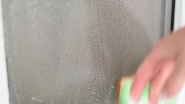 A glass opaque window being washed with a sponge and soapy water close-up. High quality 4k footage