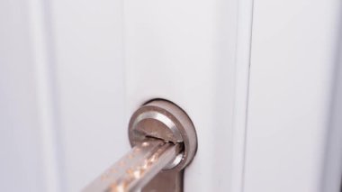 Inserting a key into a white door and turning it counterclockwise close-up. High quality FullHD footage