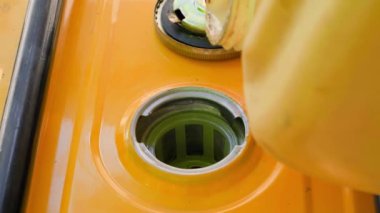 Fuel is poured into the fuel tank of a yellow gas generator from a plastic canister close-up. Refueling a gasoline generator. A jet of clear clean gasoline into the filler neck. High quality 4k