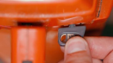 Choke lever for cold start of the engine. Preparing to launch an orange chainsaw close-up. Regulation of the air-fuel mixture. Finger pulling a gray plastic button on a blurred background. High