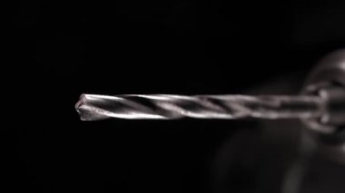 Rotation of a drill for metal in slow motion close-up on a black background. Metal rod in a drill chuck. Industrial background of a screwdriver with a drill in dark colors. professional tools. High