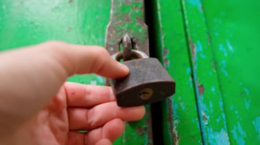 Opening a padlock on an old green garage door close-up, bottom view. The key is inserted into the keyhole and turned. Opening of abandoned premises. High quality 4k footage