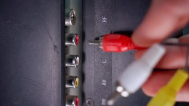 A hand inserts three colored tulip plugs into a TV close-up. RCA connection for data transfer to the screen. An outdated video and audio signal transmission standard. High quality 4k footage