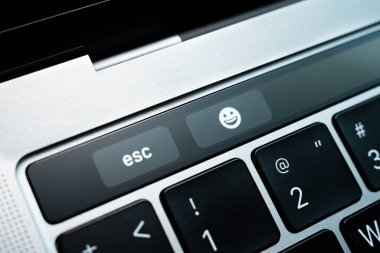 Kiev, Ukraine - August 9,2022: Touch button esc and emoji symbol on touch bar apple macbook pro close up. Additional small touch screen on a gray laptop