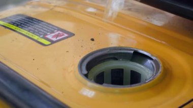 Fuel is poured into the fuel tank of a yellow gas generator from a plastic canister close-up. Refueling a gasoline generator. A jet of clear clean gasoline into the filler neck. High quality 4k