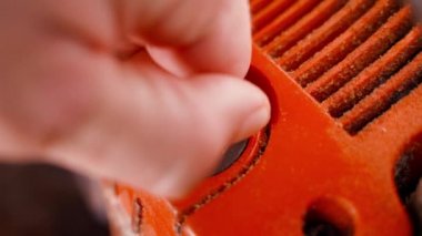 Bir el, motorlu testerenin yağlanması için yağ dolgu kapağını açar. Elektrikli testerenin aşırı ısınmasını önlemek için benzin deposu. Turuncu bir kutuda plastik bir kapağı sökmek.